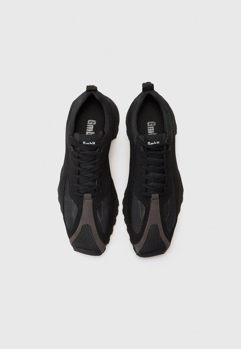 Svarta träningsskor med en meshuvuddel, texturerade ytor, kontrasterande grå detaljer och en kraftig sula, med svarta snören och varumärke.