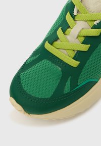 Πράσινο αθλητικό παπούτσι με πλεκτό άνω μέρος, υφασμάτινες επικαλύψεις με υφή και κιτρινοπράσινα κορδόνια. Εντυπωσιακός καμπυλωτός σχεδιασμός με ανοιχτόχρωμη σόλα.