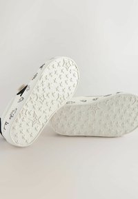White sneakers with a textured rubber sole featuring star patterns. The upper has black and white accents with various printed designs.