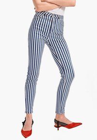 Höga skinny-jeans med vertikala blå och vita ränder. Kombinerat med röda spetsiga klackar som kompletterar denimdesignen.