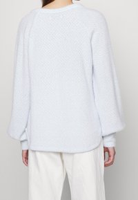 Ljusblå stickad tröja med texturerad yta, med rund halsringning och vida ärmar, sedd bakifrån.