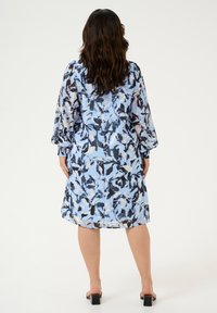 Blomstrede skjortekjole i lyseblå, sort og creme. Lange ærmer med samlede manchetter, løs pasform, knælang og letvægtsstof.