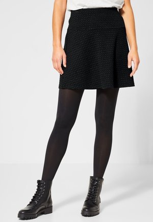 Zwarte skaterrok van gestructureerde stof, met een uitlopende snit en een hoge taille. Gecombineerd met zwarte ondoorzichtige panty's en veterschoenen.