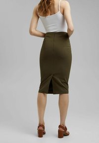 Olijfgroen getailleerde pencil skirt met een achterkant split, halflange lengte en verborgen rits. Gemaakt om te dragen met bruine hakken. Soepele stoftextuur.