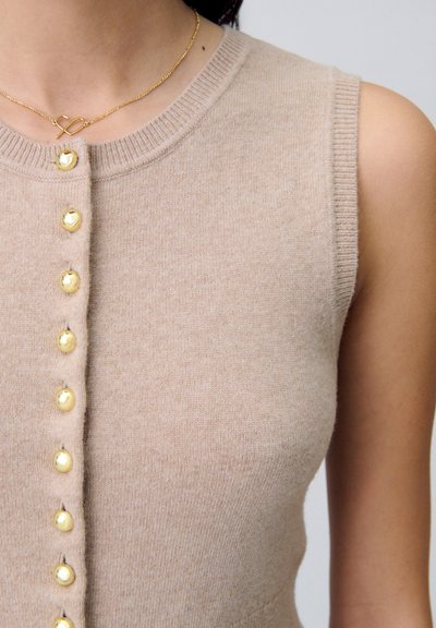 Top de punto sin mangas color beige que presenta un escote redondo y una fila de botones en tono dorado en la parte delantera. Textura suave con sutil canalé en los hombros.