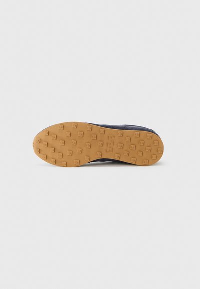 Εξωτερική σόλα παπουτσιού από καφέ καουτσούκ με υφή που βελτιώνει την πρόσφυση, διαθέτει εξαγωνικούς καρφίτσες για καλύτερο κράτημα και ομαλή σκοτεινή επάνω επιφάνεια.