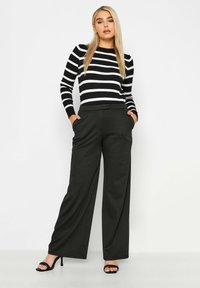 Gestreepte zwart-witte top met lange mouwen, slim fit en ronde hals, gecombineerd met hoge taille, wijde zwarte broeken en open teen hakken.