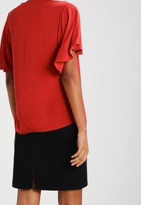 Blouse rouge à manches courtes avec des manches à volants, associée à une jupe en denim noire avec une fente centrale et des poches avant.