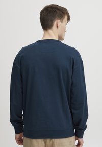 Tamnoplav pulover iz mehkega materiala, z okroglim izrezom, dolgimi rokavi in rebrastimi manšetami. Enostaven dizajn brez vidnih vzorcev.