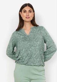 Svetlozelený top s dlhým rukávom s čiernym paisley vzorom. Design s výstrihom do V, voľný strih a hladká textúra. Skombinovaný s zodpovedajúcimi nohavicami.