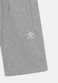 Grå bomullsshorts med elastisk midja, snörning och en vit broderad Adidas-logotyp på nedre vänstra sidan.