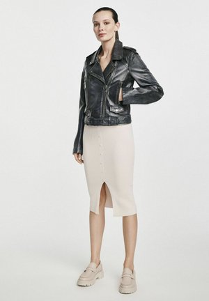 Czarna skórzana kurtka motocyklowa, żeberkowa beżowa spódnica midi z guzikami z przodu oraz jasne mokasyny z grubą podeszwą.