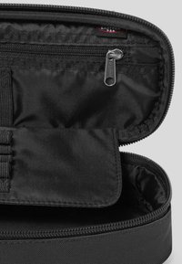 Custodia in nylon nera con chiusura a zip, dotata di una tasca interna e cinturini elastici. Texture liscia, forma rettangolare compatta.