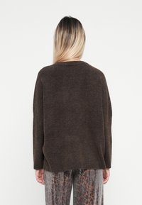 Bruine, gestructureerde trui met een ontspannen pasvorm, geribde halslijn en verlaagde schouders, gedragen met gestreepte, contrasterende broek.
