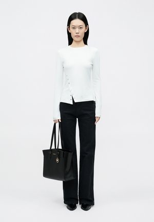 Haut blanc à manches longues avec détails à boutons-pression, associé à un pantalon noir évasé et un sac fourre-tout noir avec des détails dorés.
