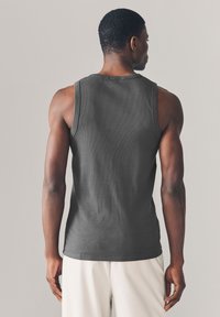 Débardeur gris foncé à côtes avec un col arrondi, coupe ajustée et larges emmanchures, vu de dos sur un mannequin.