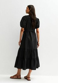 Zwart gelaagd maxi-jurken met pofmouwen, met een cinch taille en een vloeiende rok. Draagt met sandaaltjes met bandjes.