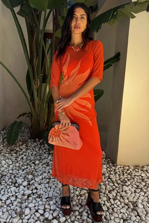 Rød midi-kjole med blomsterdesign i en lysere nyanse, kombinert med en utsmykket korall clutch og svarte plattform sandaler.