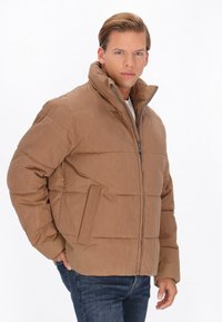 Bruine pufferjack met hoge kraag, ritssluiting en zijzakken. Heeft een gewatteerd patroon en een gladde, matte textuur.