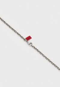 Catena in metallo argento con maglie lisce e interconnesse e un'etichetta rossa con la scritta "HUGO". Presenta un gancio per la chiusura.