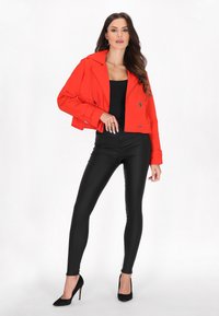 Rød cropped jakke med dobbelte knapper, sort bodysuit, sorte tætsiddende leggings og sorte spidse hæle. Glat stof, skræddersyet design.