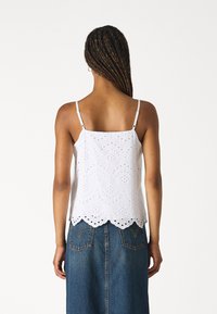 White sleeveless top with eyelet detailing, scalloped hem, and adjustable straps, paired with a denim skirt featuring back pockets.