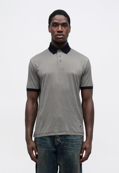 Tamsiai pilkas polo marškinėlis su tekstūruotu raštu, juoda apykakle ir trimis mygtukais priekyje. Derinamas su laisvalaikio mėlynomis džinsinėmis kelnėmis.