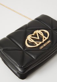 Black quilted leather crossbody bag with gold chain strap and gold Love Moschino logo plaque on front flap.