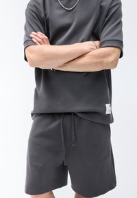 Donkergrijs gecoördineerd set bestaande uit een sweatshirt met korte mouwen en shorts, beide gemaakt van zachte stof met frontzakken en een labeldetails.