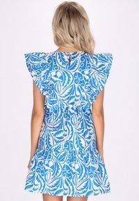 Rochie scurtă albastră cu mâneci volane, având un model floral alb în spirală. Spatele are o deschidere mică la gât și un tiv stratificat.