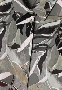 Camicia con bottoni dal motivo camouflage astratto nei toni del grigio, nero, beige e bianco, con colletto a punta.