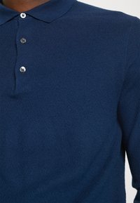 Polo à manches longues texturé bleu marine avec trois boutons visibles sur la patte de boutonnage.