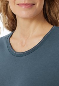 T-shirt turchese con collo rotondo, caratterizzato da una cucitura in contrasto rosa lungo il bordo. Tessuto morbido e liscio con forma aderente.
