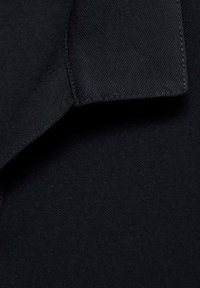 Svart texturerad tyg med en slät krage. Materialet verkar hållbart och flexibelt, med en ren och enkel design.