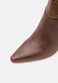 Gros plan d'une botte en cuir marron à bout pointu avec une partie supérieure texturée à motif crocodile.
