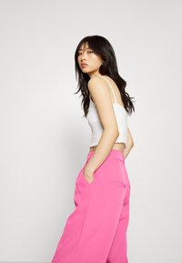 Top de alças finas cortado branco combinado com calças rosa de cintura alta e perna larga. As calças apresentam bolsos laterais e uma textura suave.