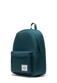 Sac à dos en tissu teal avec une forme arrondie, poche avant et poignée supérieure. Il présente un logo en bas à l'avant. Texture lisse.