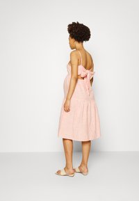 Vestido listrado em rosa claro e branco, com corpete justo, recorte nas costas e detalhe de laço oversized. Saia midi fluida, usado com sandálias neutras.