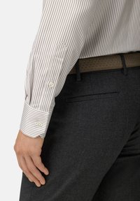 Pruhované dlouhé rukávy v bílé a hnědé barvě, s knoflíkovými manžetami. Šedé kalhoty s jemnou strukturou a hladkým páskem viditelným nad pasem.