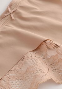 Tejido beige con borde de encaje y textura suave, con un delicado lazo cerca de la cintura. El material suave crea un efecto de capas.