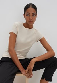 Beige ribbed short-sleeve top with a round neckline, paired with black cropped pants. Smooth texture, fitted design, simple and clean aesthetic.
