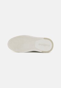 La semelle de la chaussure Gioseppo est fabriquée en caoutchouc lisse de couleur blanc cassé, avec des rainures horizontales et diagonales pour une meilleure adhérence, et le logo en relief près du talon.