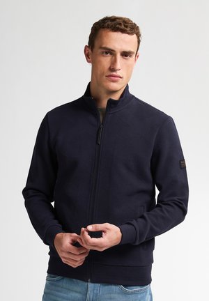 Marine zip-up jack met een gestructureerde stof met een diamantpatroon, voorzien van een hoge kraag en ribboorden. Eenvoudig ontwerp met minimale accenten.