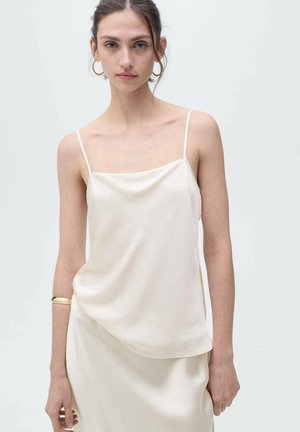 Light cream camisole with thin straps; soft, smooth fabric; relaxed fit; subtle draping; paired with a simple skirt; minimalist design.