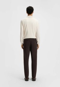 Chemise blanche à manches longues associée à un pantalon marron, avec une coupe décontractée. La chemise possède un col rond ; le pantalon a des poches arrière.