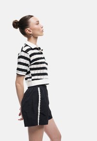 Polo en tricot rayé noir et blanc à manches courtes, associé à un short noir avec un détail de dentelle blanche sur le côté.