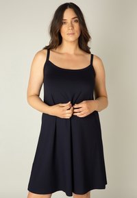 Marineblauwe mouwloze jurk met een ronde hals, flared vorm en zachte stof. Heeft dunne banden en een relaxte pasvorm.