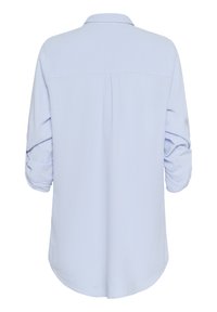 Chemise bleu clair avec une texture douce, manches longues retroussées, empiècement dos et ourlet arrondi. Design minimaliste, tissu léger.