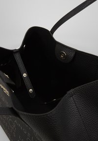 Sort læder tote taske med en struktureret overflade, der har en tryklås, to håndtag og en velorganiseret indvendig med lommer.