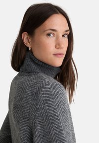 Maglione a collo alto grigio in tessuto a spina di pesce, con colletto a coste. Texture morbida, vestibilità rilassata e dettagli di motivo sottili sul tessuto.